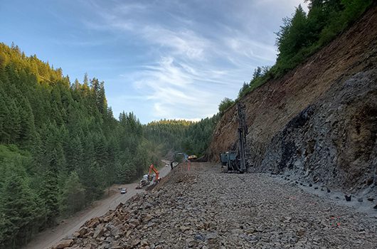 Equipment on a trail above US-95 in Culdesac Canyon helps with rock removal to extend the passing lane.