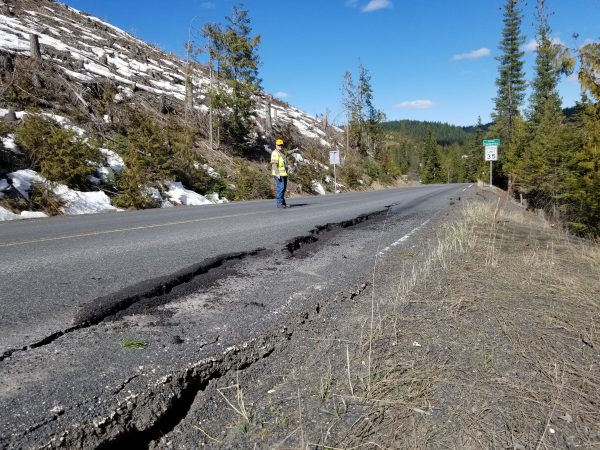 A man stands on the highway where the shoulder is starting to sink