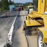 A broomer follows a truck putting down sand