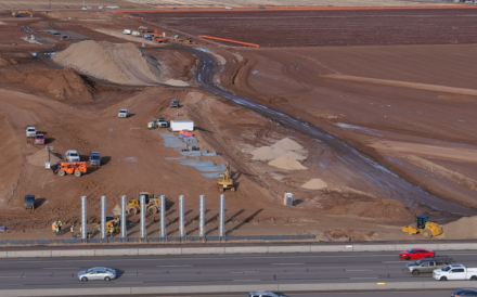 Cars drive by a staging area for the new highway 16 construction.