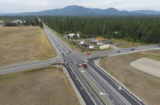 overhead view of the intersection of SH-53 and Ramsey. Orange cones can be observed along one edge of new pavement. The traffic lights are strung at a 45-degree angle across the intersection