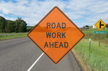 A road work ahead sign superimposed over a roadside view of US-95 near the Aht'Wy interchange project.