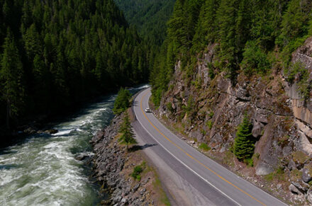 A bend in the highway with mountains on the right and a river on the left.
