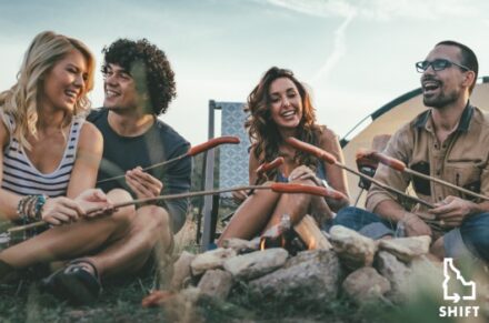 Four people roasting hotdogs over a camp fire.