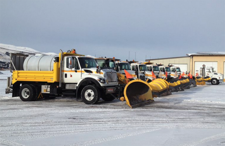 A line of snowplows parked in a yard.