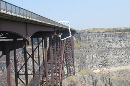 An Under Bridge Inspection Truck (UBIT) hangs over the Perrine Bridge US 93