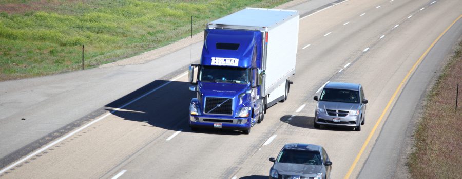 A blue semi truck and two cars driving on the interstate.