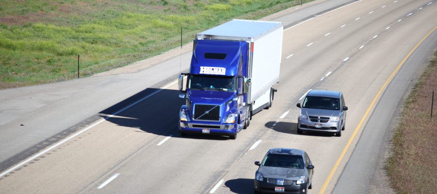 A blue semi truck and two cars driving on the interstate.