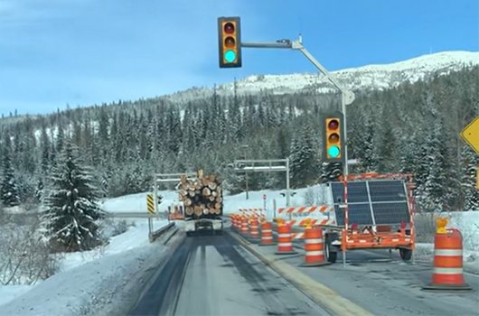 Log truck passing over bridge on SH-3 under a temporary traffic signal