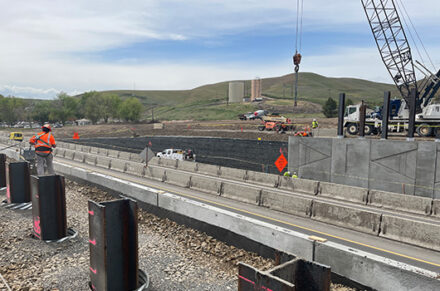 Crews place concrete panels with a crane at the US-95 Aht'Wy Interchange.