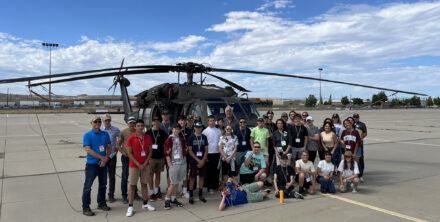 A group of people pose for a picture in front of a helicopter.