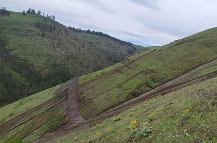 State Highway 64 on a steep slope. A storm has caused erosion and mud is spilling across the road.