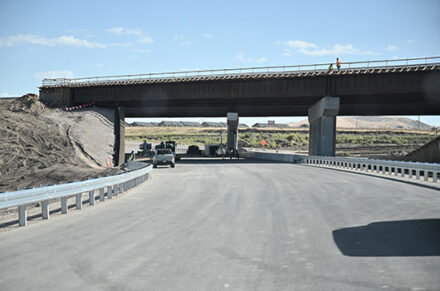Cars drive under an under construction overpass.