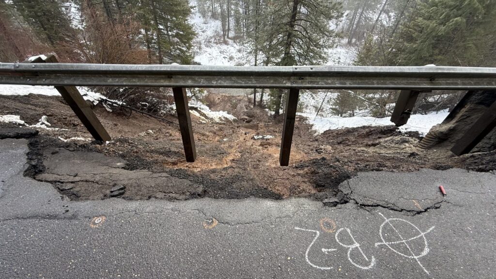 A guardrail and crumbled road with a steep downhill slope in the background.