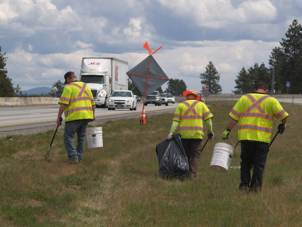 Three people picking up trash on the side of I-90