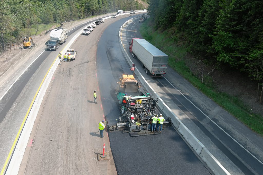 Crews paving the inside lanes of I-90 while a single lane of traffic passes on either side.