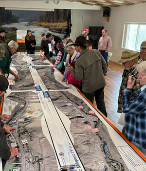 A large map takes up several tables and community members view the route.