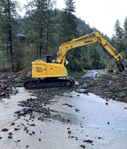 An excavator in the foreground is clearing debris from SH-162 after major floods in 2024.