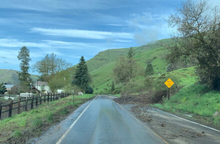 A view of SH-162 with muddy debris flooding across the roadway.