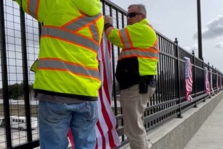 Workers hang American flags on a railing.
