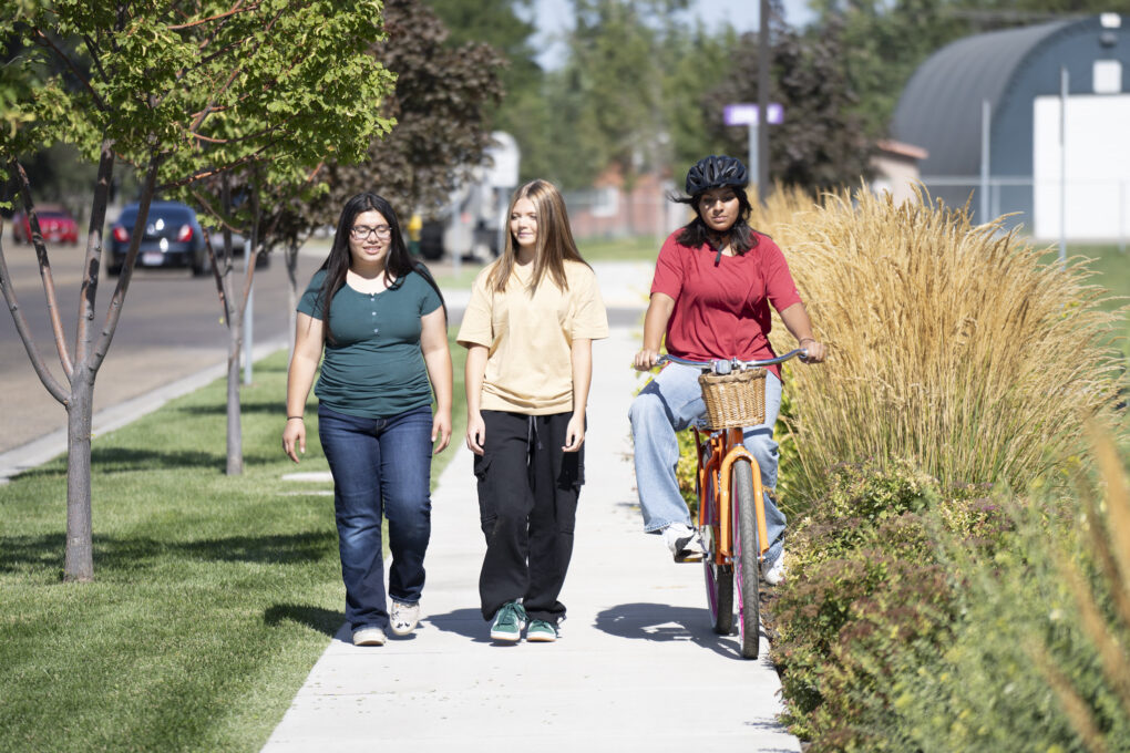 Three young women. Two are walking and one is on a bike.