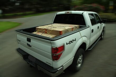 White truck with boxes securely tied down in truck bed.