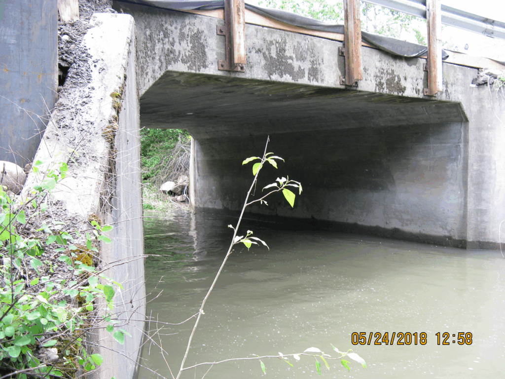 A square concrete culvert with a creek running through it.
