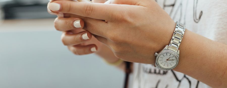 Woman with off-white painted nails holding phone in both hands. Her thumbs are poised over the keys.