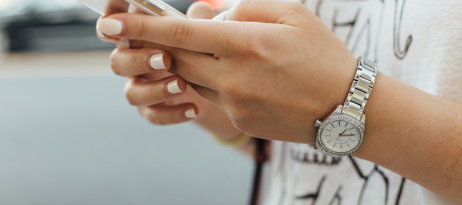 Woman with off-white painted nails holding phone in both hands. Her thumbs are poised over the keys.