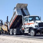 A dump truck and paver working on repaving a road.