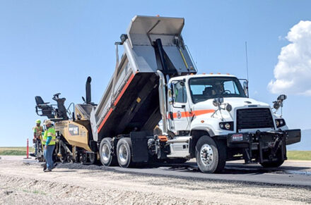 A dump truck and paving machine repaving a section of a road.