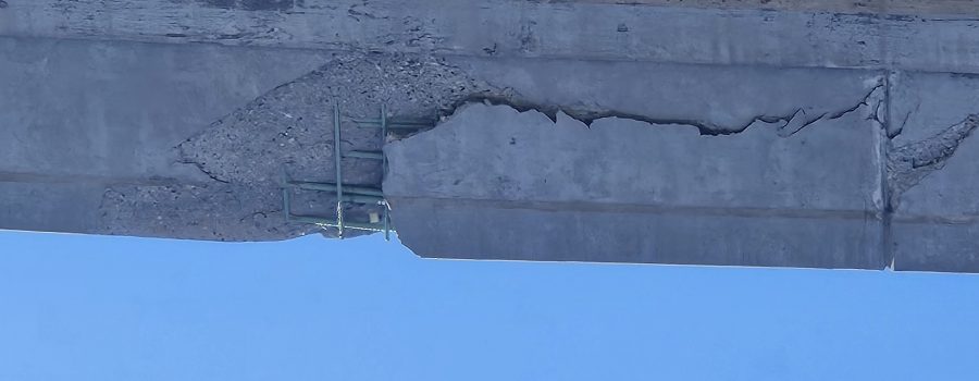 Picture of significant concrete damage on a highway overpass.