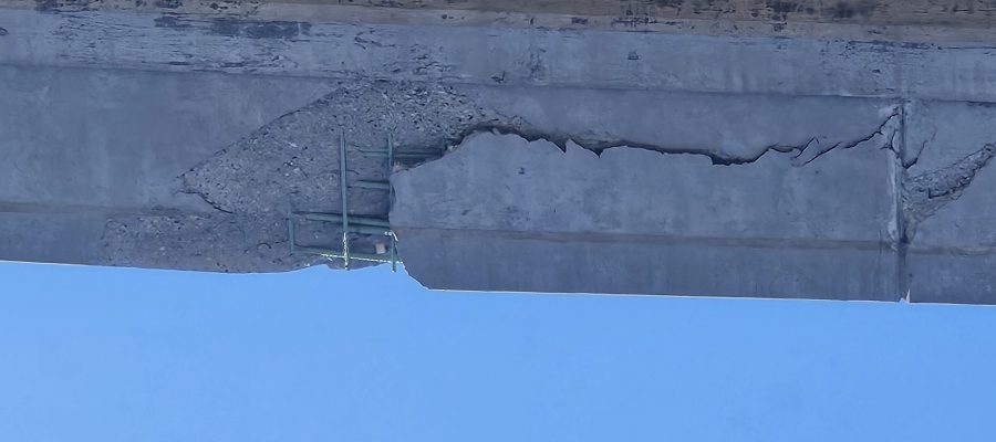 Picture of significant concrete damage on a highway overpass.