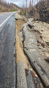 Edge of road being washed away by creek causing road damage on rural road through woods