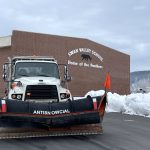 Snowplow positioned outside a school with the name "Antisnowcial" on the blade.