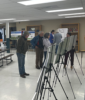 Community members looking at display boards on easels at a public meeting.