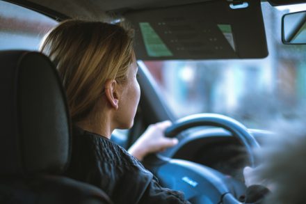 Young woman with blonde hair driving a car, both hands on the steering wheel, focused on the road ahead
