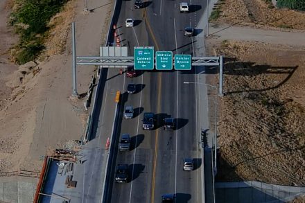 Aerial view of traffic traveling across a bridge on State Highway 55 in Nampa, passing under overhead signs for I-84 west to Caldwell and Ontario, Midland Boulevard north, and the Karcher Bypass.
