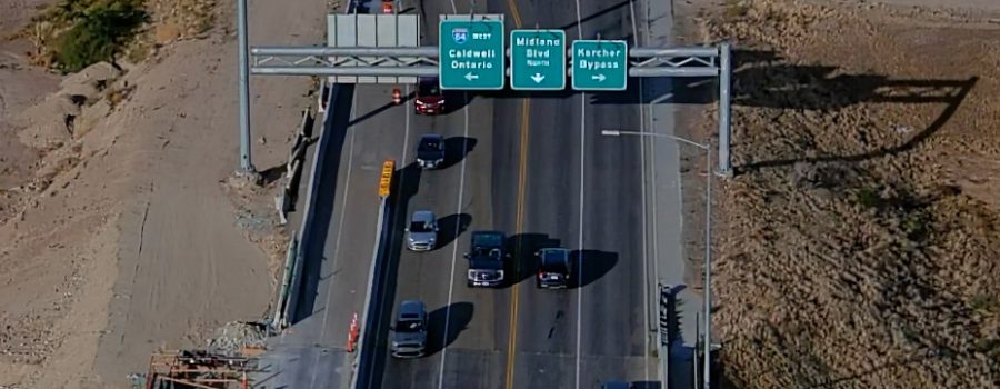 Aerial view of traffic traveling across a bridge on State Highway 55 in Nampa, passing under overhead signs for I-84 west to Caldwell and Ontario, Midland Boulevard north, and the Karcher Bypass.