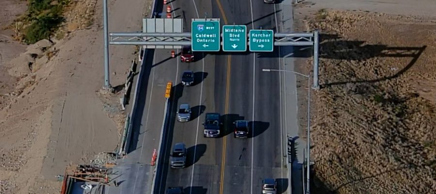 Aerial view of traffic traveling across a bridge on State Highway 55 in Nampa, passing under overhead signs for I-84 west to Caldwell and Ontario, Midland Boulevard north, and the Karcher Bypass.