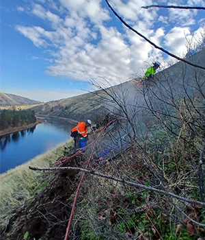 A view of two workers installing anchors near the top of the slope for the US-12 emergency rock scaling project by Arrow bridge.