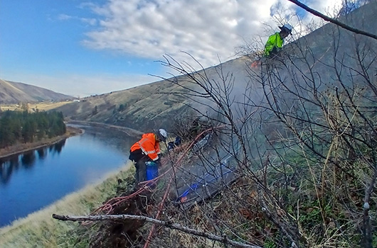 A view of two workers installing anchors near the top of the slope for the US-12 emergency rock scaling project by Arrow bridge.