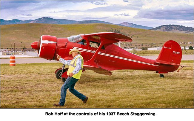 Bob Hoff stands near his red airplane, pointing towards the sky