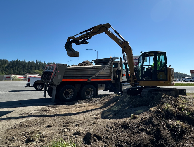 A loader dumps a bucket full of dirt into a dump truck nearby. 