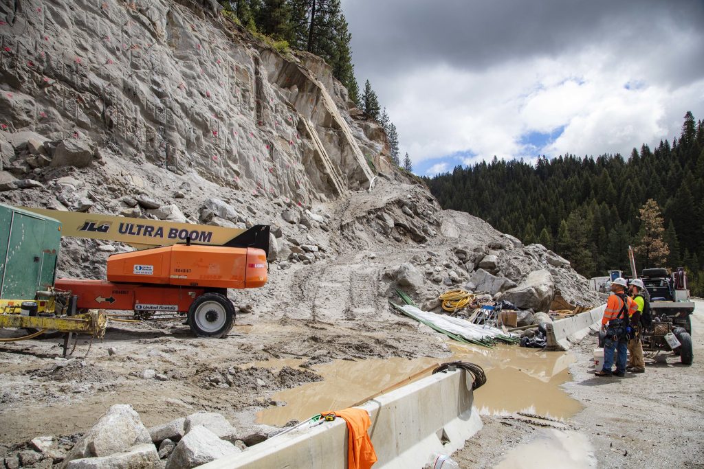 Two workers stand and observe a construction zone on a hillside.
