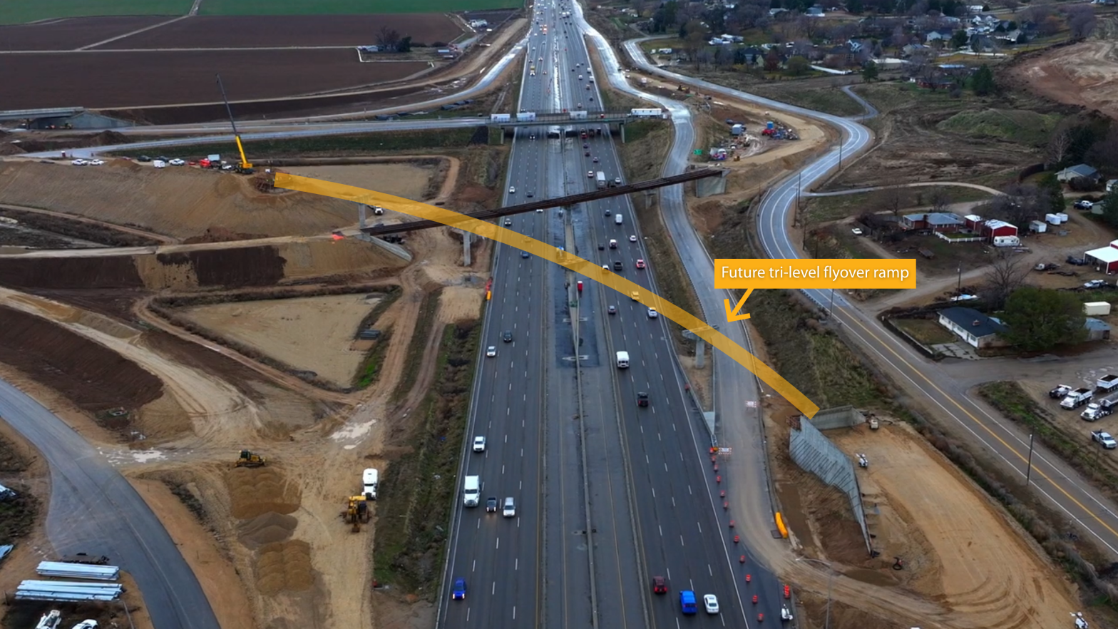 Aerial view of Interstate 84 with active traffic and surrounding construction. A highlighted graphic overlays the image, illustrating the future SH-16 tri-level flyover ramp crossing above I-84, with bridge supports and earthwork visible below.