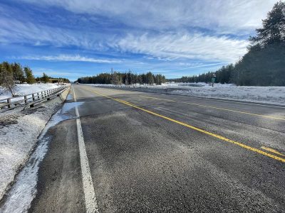 Roadside view of US-20 facing north at the Buffalo River Bridge near Pond's Lodge in Island Park, Idaho, with the river and forest in the background.