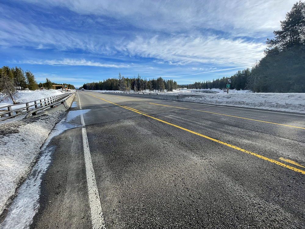 Roadside view of US-20 facing north at the Buffalo River Bridge near Pond's Lodge in Island Park, Idaho, with the river and forest in the background.