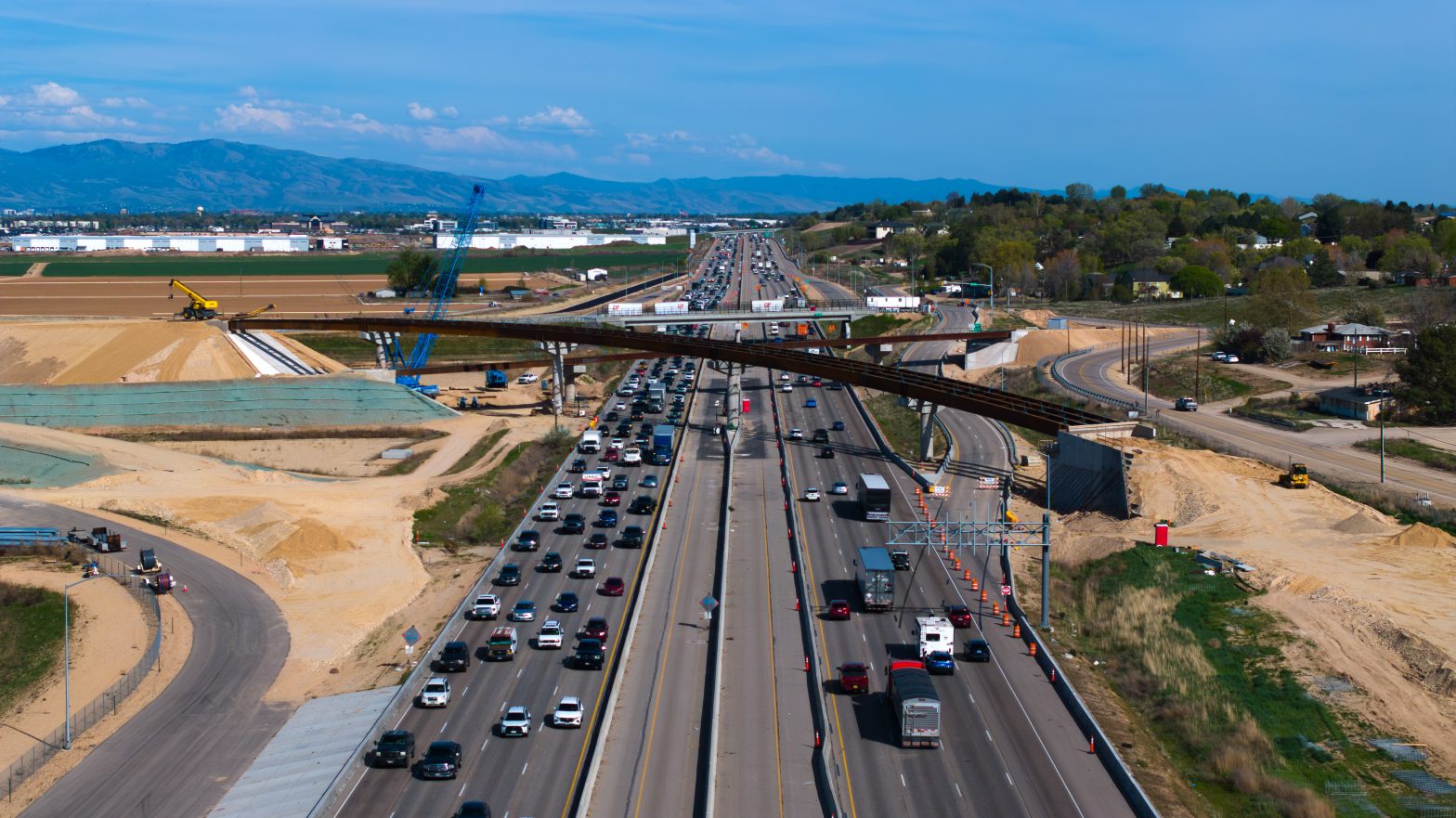 Aerial view of heavy traffic on Interstate 84 near a construction zone, with an overpass under construction and lane closures marked by orange cones.