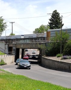 Southbound traffic on the US-26 Yellowstone Highway underpass in Idaho Falls, showing a train passing on the railroad tracks overhead.
